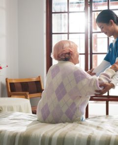 Senior woman, caregiver and help on bed with care, assisted living and support in nursing home. Elderly patient, nurse and mobility aid in bedroom for friendly service, healthcare and consulting