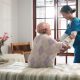 Senior woman, caregiver and help on bed with care, assisted living and support in nursing home. Elderly patient, nurse and mobility aid in bedroom for friendly service, healthcare and consulting